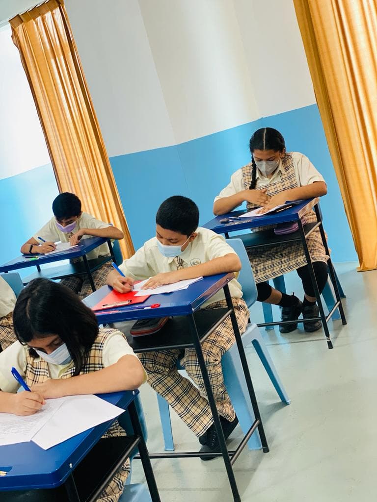 Students writing at blue desks in a bright classroom