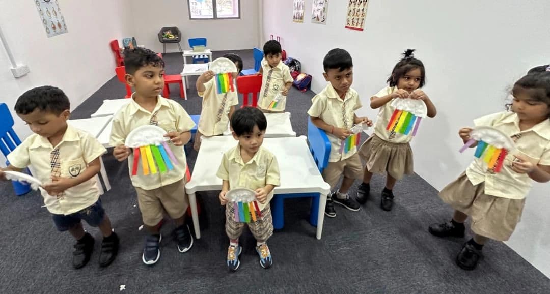 Young children in uniform holding rainbow-coloured paper