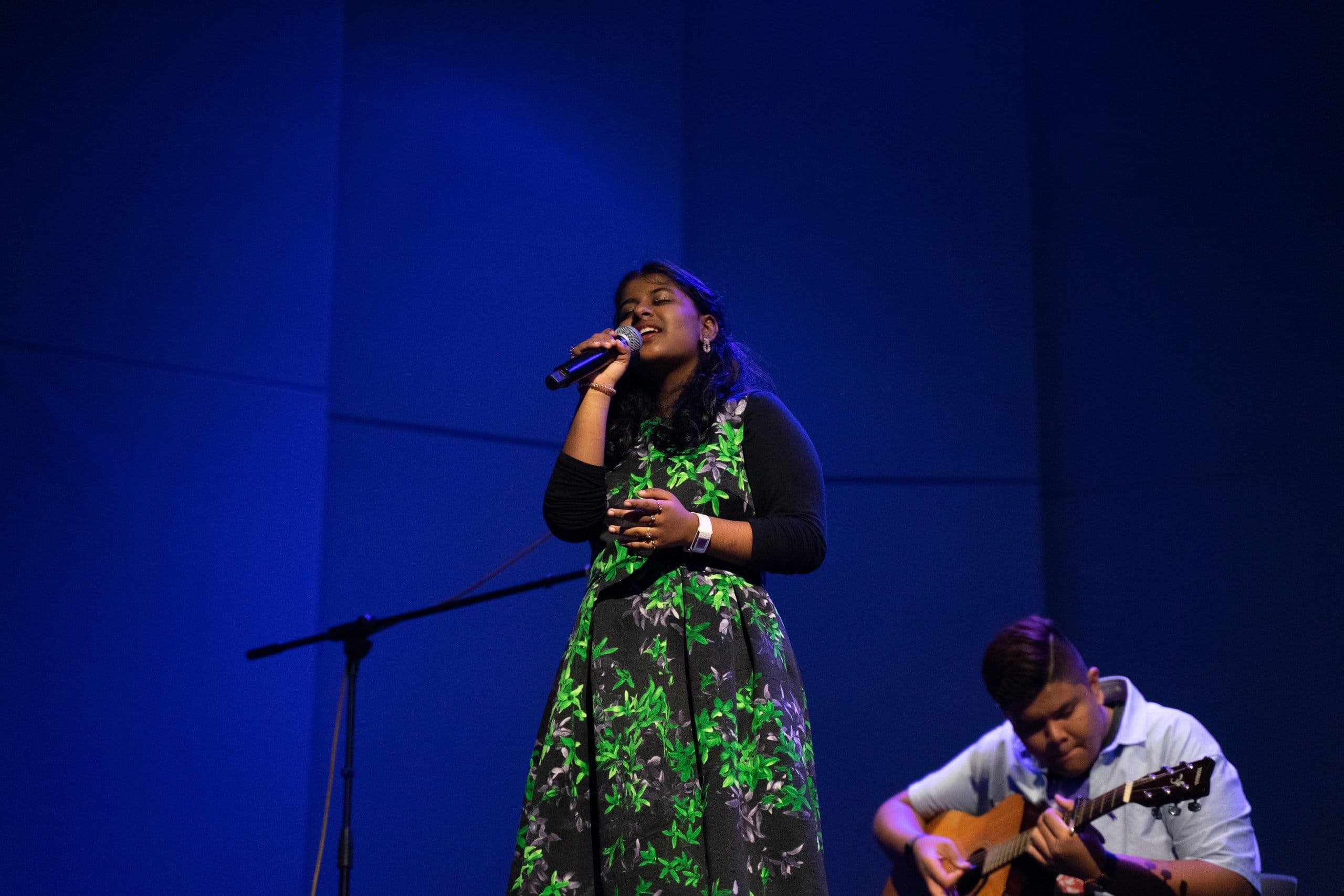 A student singing on stage with a guitarist